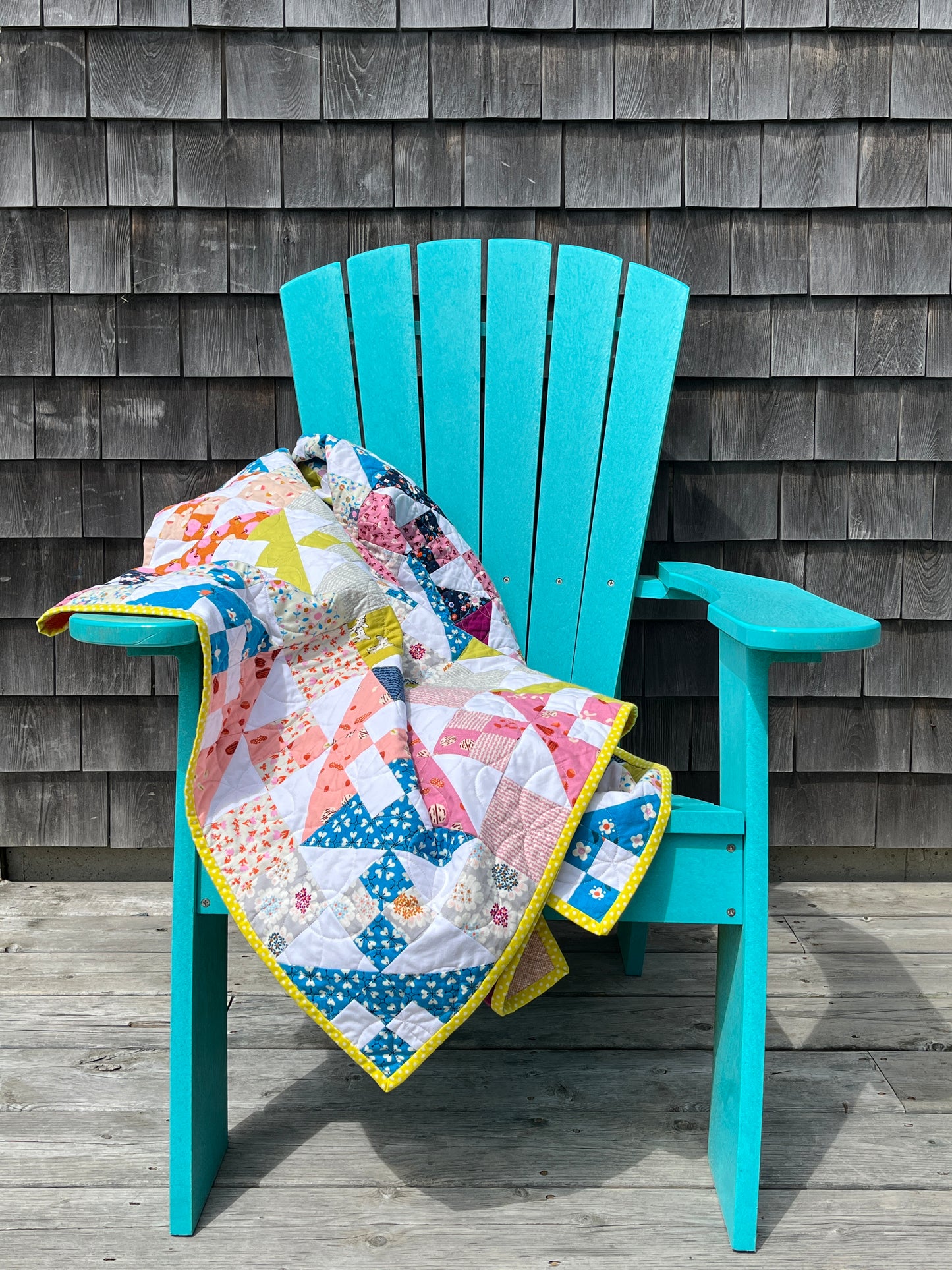 Turquoise chair with a colorful quilt draped over it on a wooden deck.